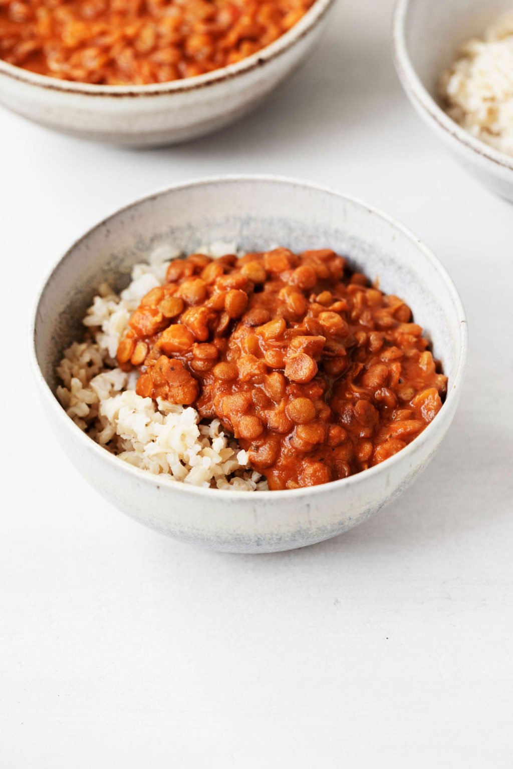 Two white, ceramic bowls hold dishes of garam masala spiced lentils and cooked brown rice.