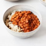 Two white, ceramic bowls hold dishes of masala spiced lentils and cooked brown rice.