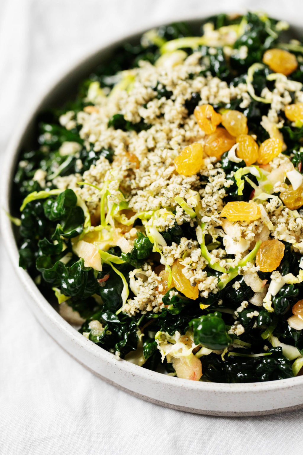 A large serving plate with a plant-based salad, which is topped with golden raisins and hemp seeds.