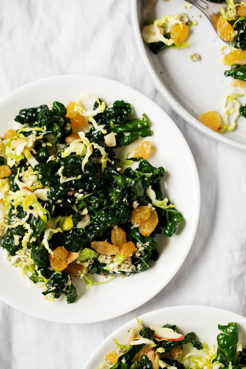 A few serving plates of a wintery vegan Brussels sprout kale salad, topped with golden raisins.