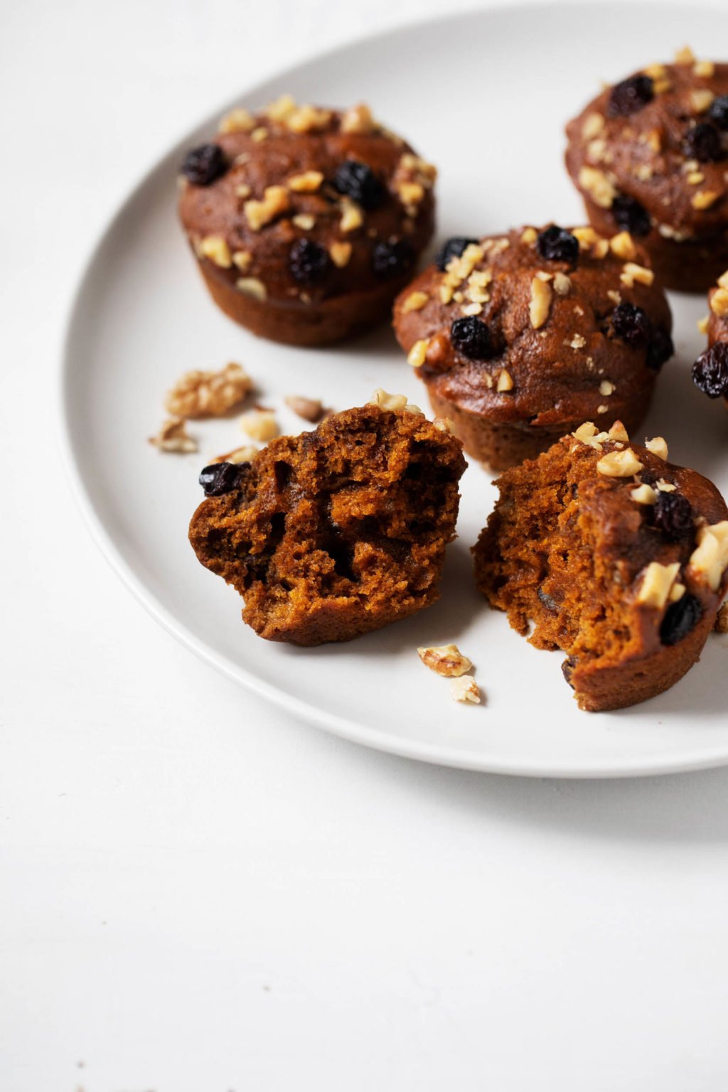 A plate with four vegan pumpkin gingerbread spice muffins, ready to be split apart and eaten.