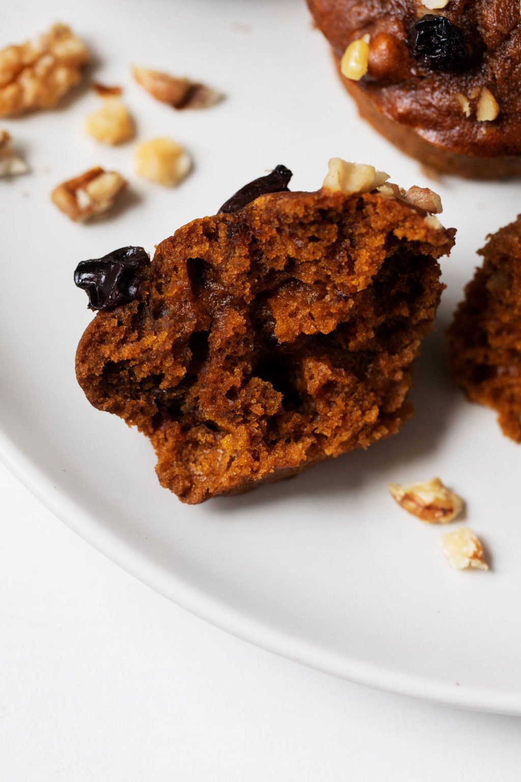 Half of a vegan pumpkin muffin with gingerbread spices, resting on a place with chopped walnut pieces.