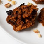 Half of a vegan pumpkin muffin with gingerbread spices, resting on a place with chopped walnut pieces.