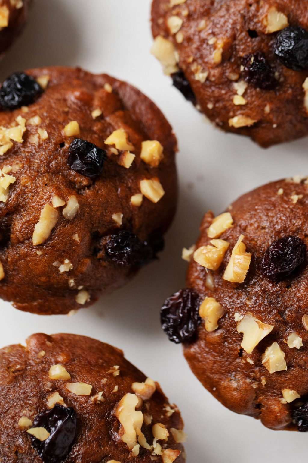 A top down view of vegan gingerbread muffins, topped with raisins and chopped walnuts.