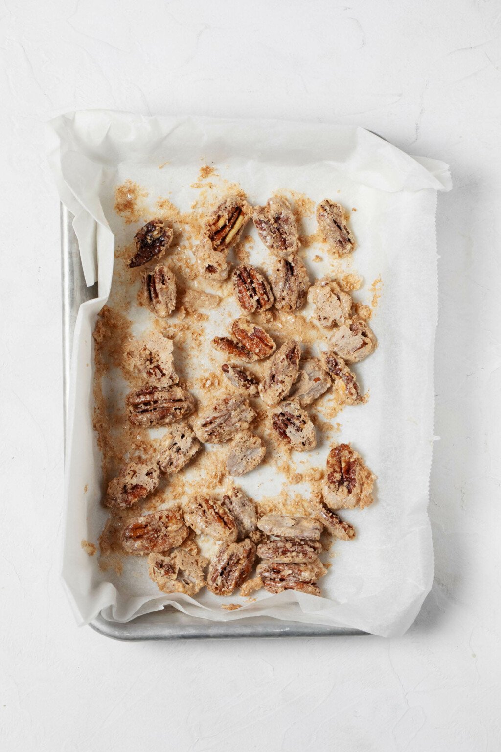 An overhead image of a small baking tray, which is covered with vegan candied pecans.