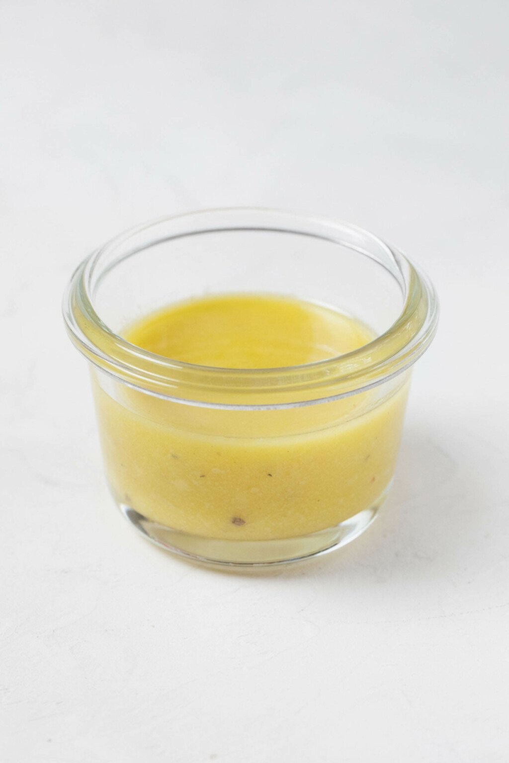 A small, round container of vinaigrette rests on a white surface.