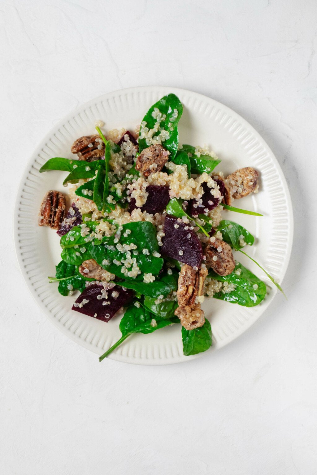 An overhead image of a round, rimmed white plate, which is serving a vegan quinoa and beet salad with crispy pecans.