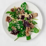 An overhead image of a round, rimmed white plate, which is serving a vegan quinoa and beet salad with crispy pecans.