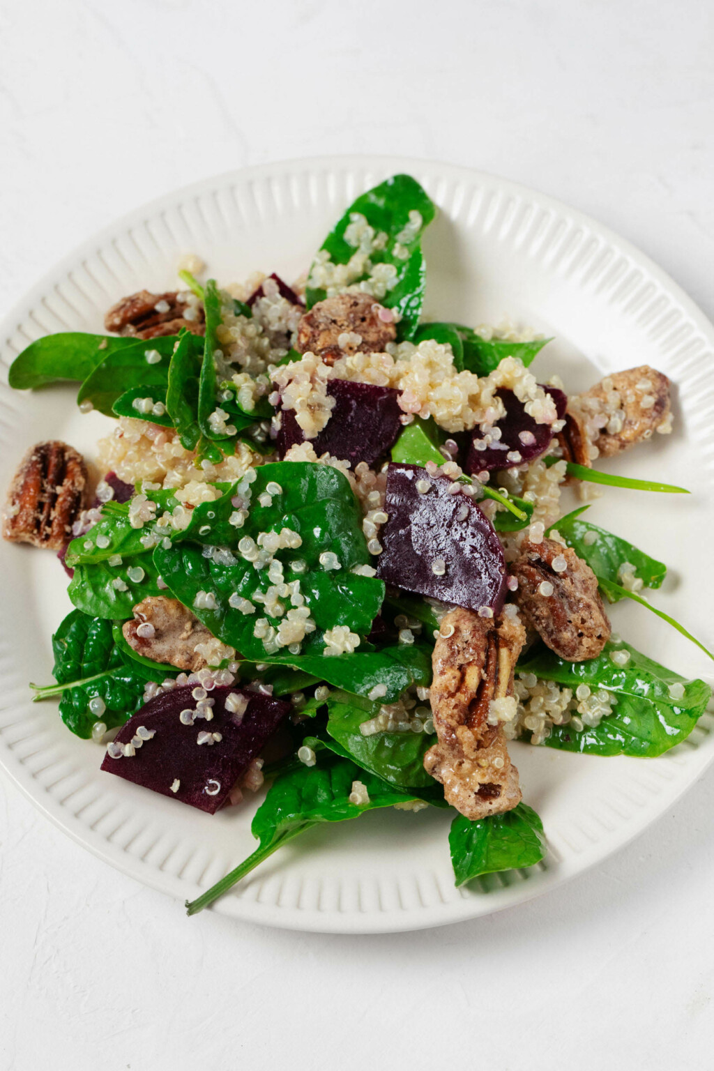 An overhead image of a round, rimmed white plate, which is serving a vegan quinoa and beet salad with crispy pecans.
