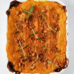 A small, rectangular baking dish is filled with a vegan sweet potato lentil shepherds pie.