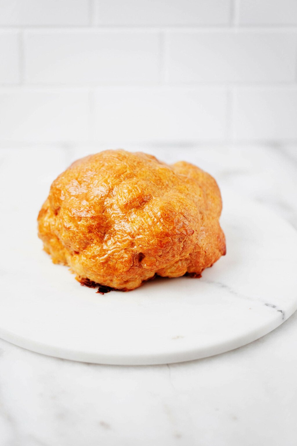 Whole roasted lemon tahini cauliflower is resting on a round, marble serving platter. The platter is on a white surface.