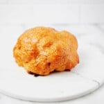 Whole roasted lemon tahini cauliflower is resting on a round, marble serving platter. The platter is on a white surface.