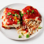 Two stuffed cabbage rolls are laid out, side by side, on a plate. One has been cut into and the filling is spilling out.