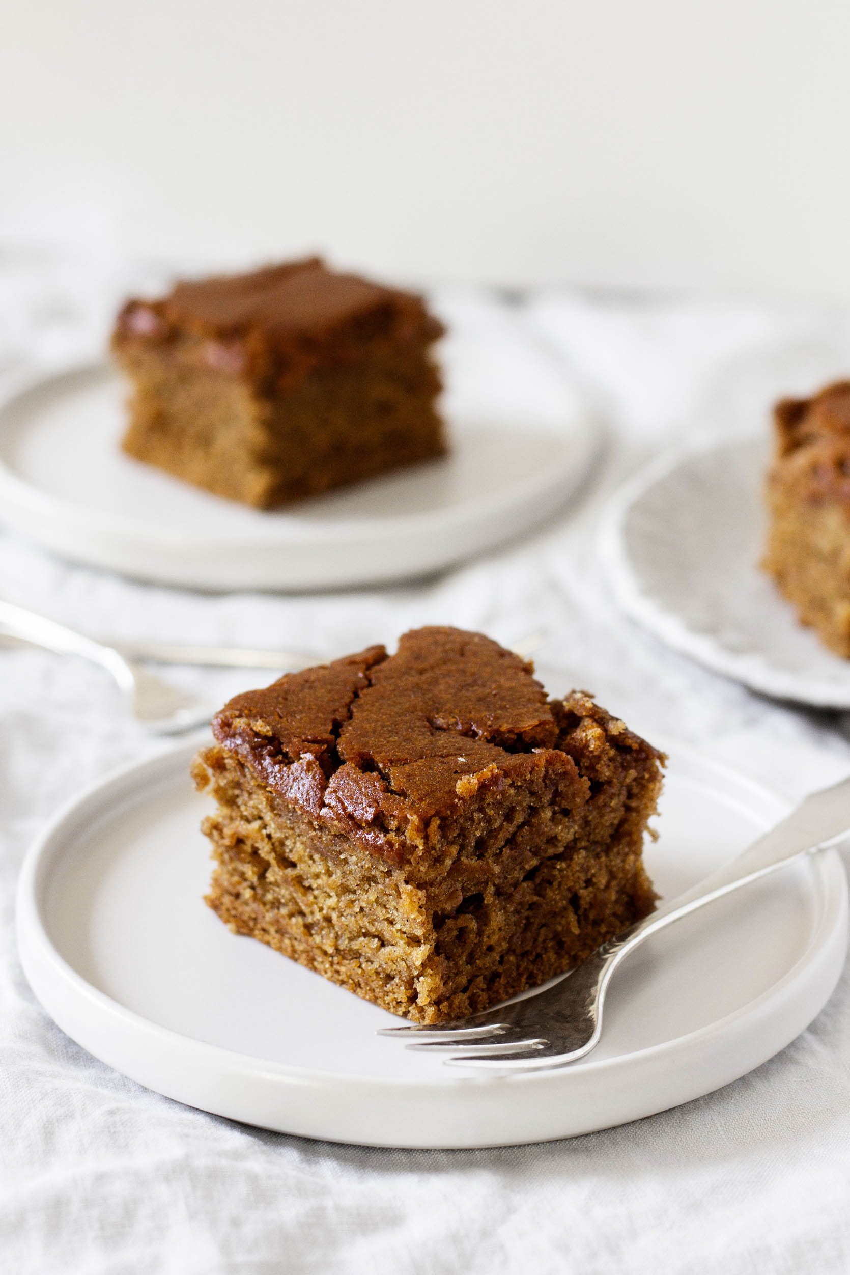 Several dessert plates are topped with squares of gingerbread and accompanied by dessert forks.