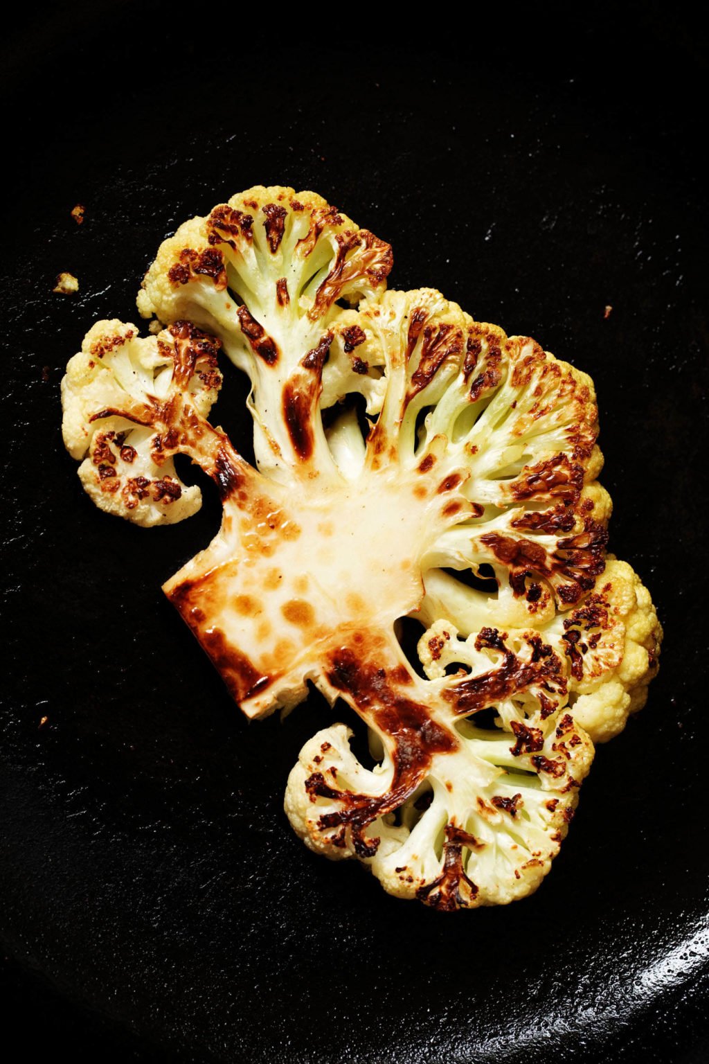 A black, cast iron skillet holds a piece of seared, browning cauliflower.