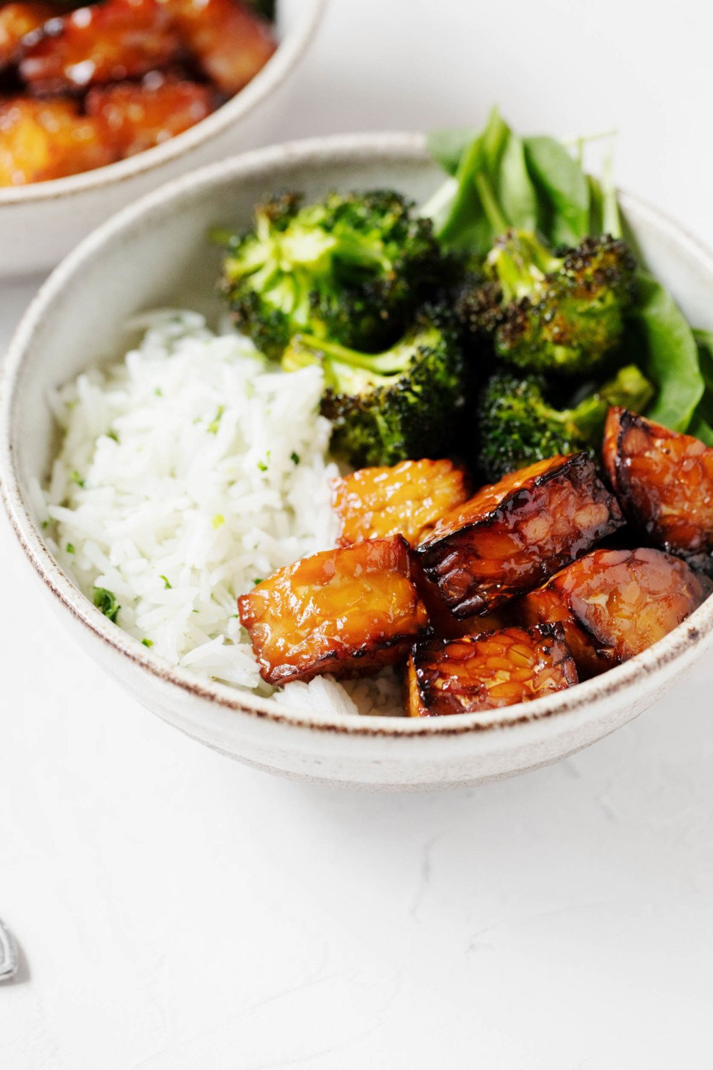 A ceramic bowl has been piled high with plant based ingredients, including cooked rice, a protein, and greens.
