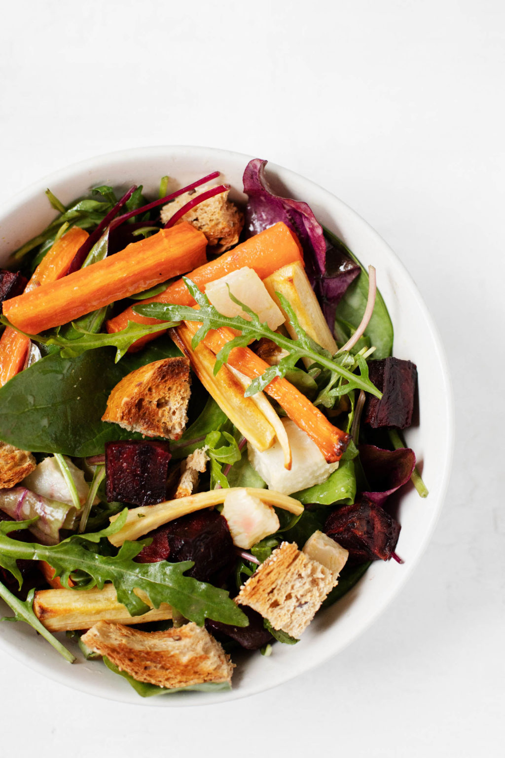 A round bowl containing the colorful ingredients of a wintertime salad, including greens, carrots, parsnips, and beets.