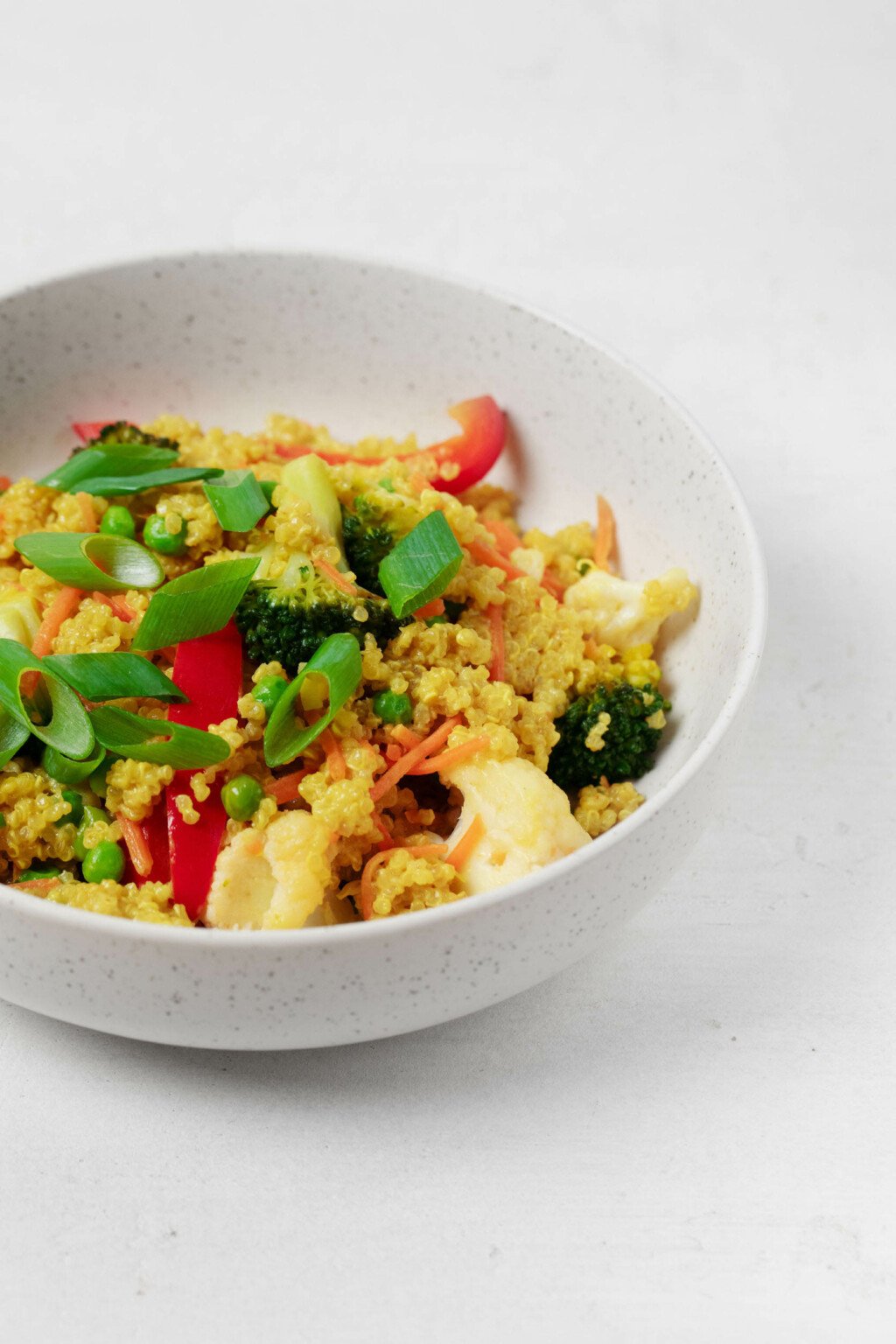 A closeup photograph of a bowl of creamy curried quinoa, which has been topped with crisp, green scallions.