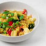 A closeup photograph of a bowl of creamy curried quinoa, which has been topped with crisp, green scallions.