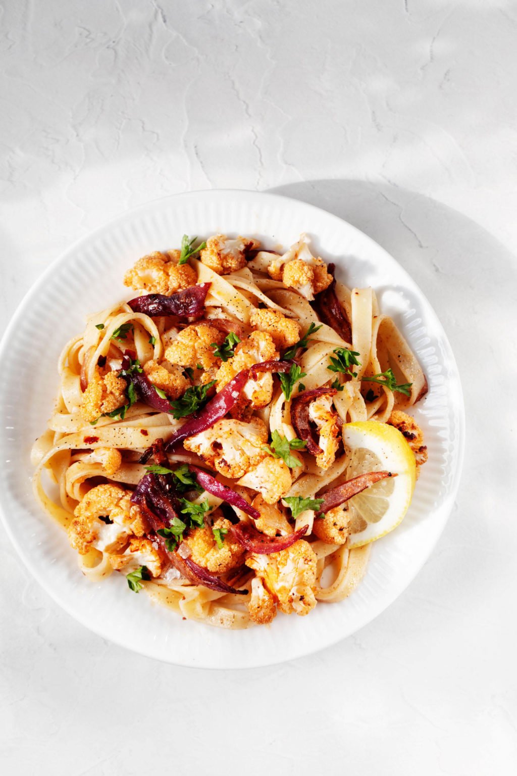 An overhead image of a plant-based pasta dish that has been prepared with lots of vegetables. It's garnished with a sprinkle of green parsley.