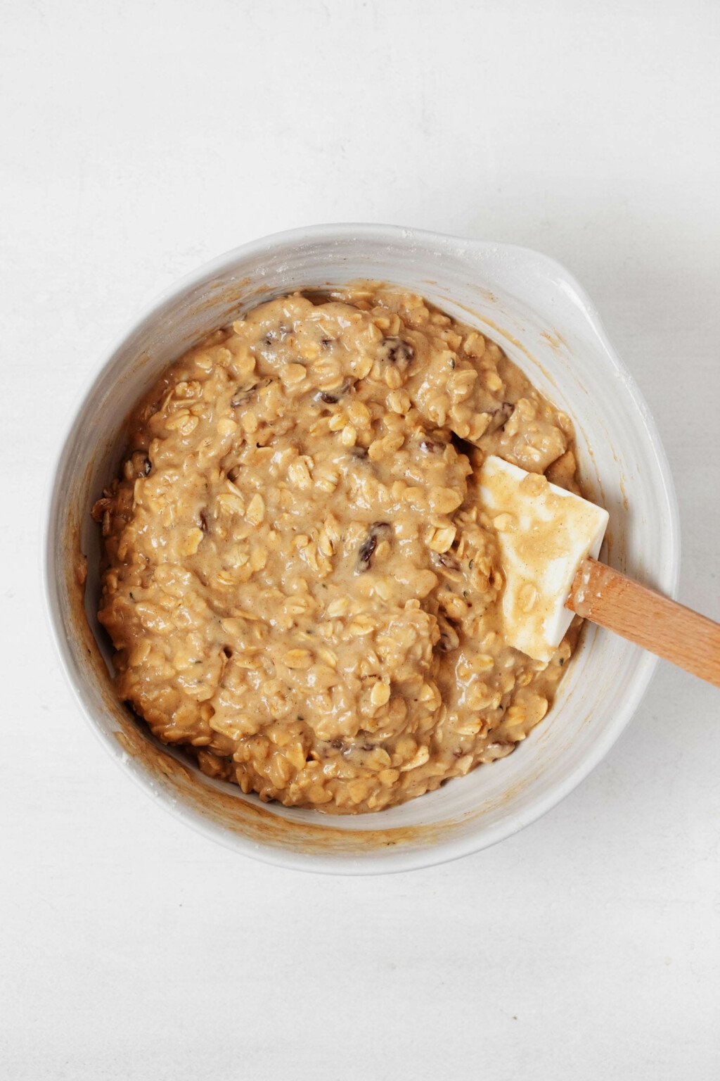The batter for something is being mixed in a white bowl, with a spatula. It rests on a white surface.