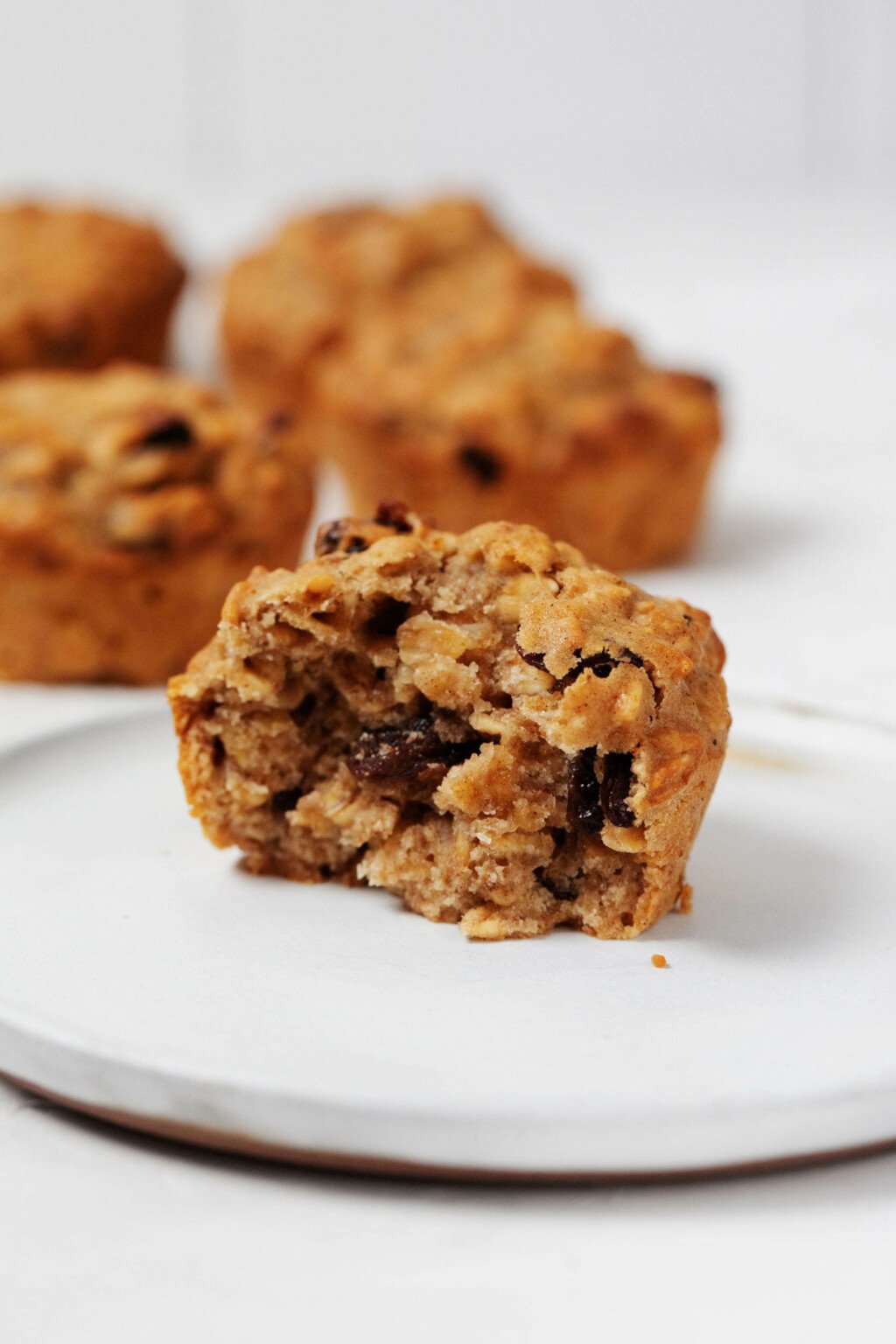 A vegan breakfast treat, made with rolled oats and raisins, is broken in half and resting on a small, white plate.