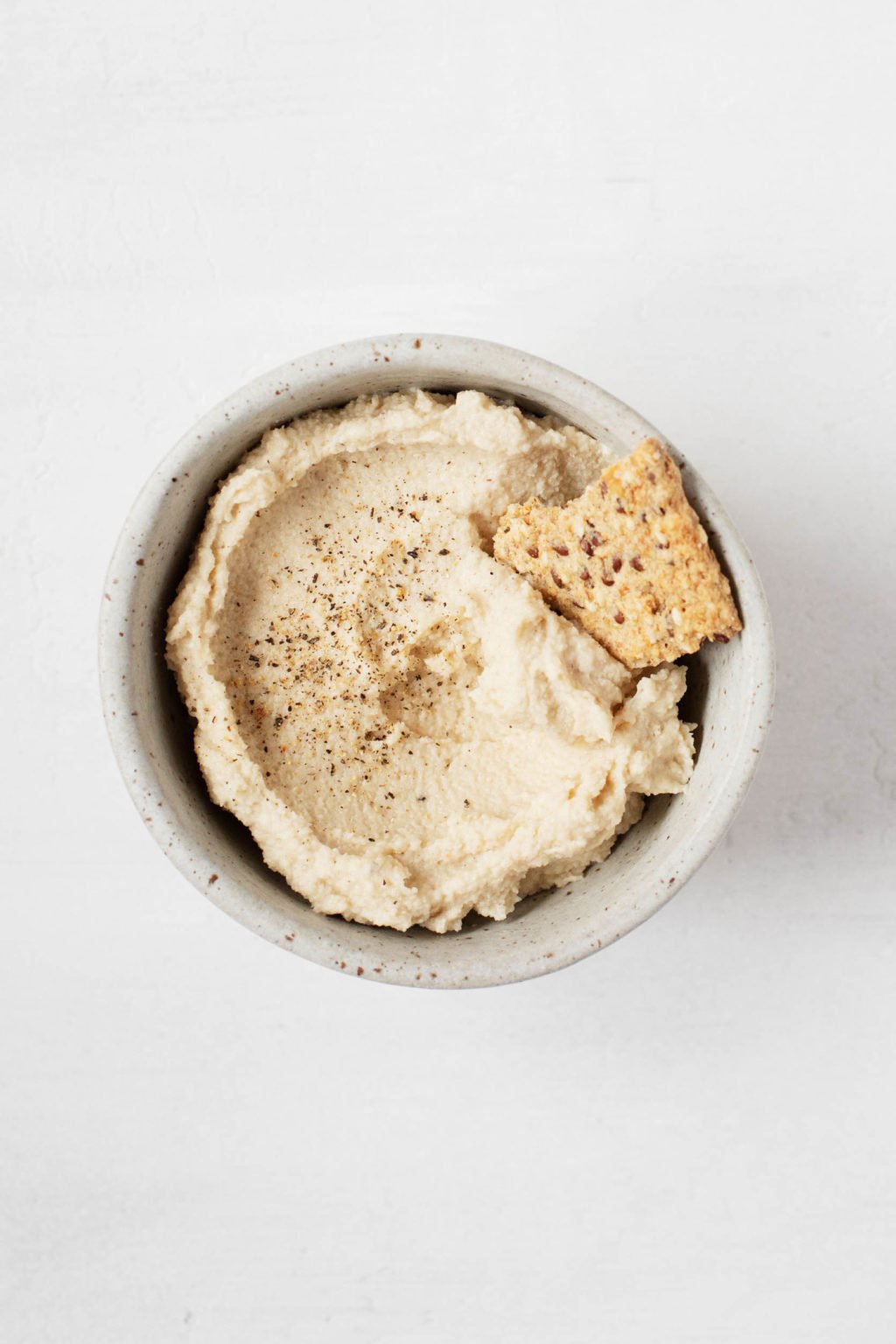 A small bowl is filled with dairy-free cheese spread and a whole grain cracker.