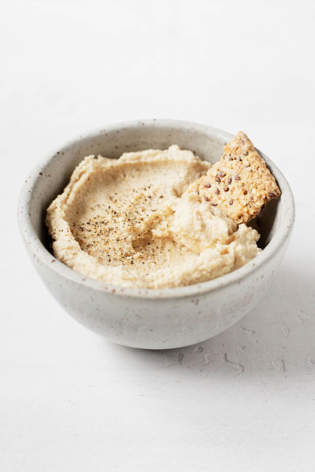 A small ceramic bowl holds a creamy vegan cashew cheese and a cracker for dipping.