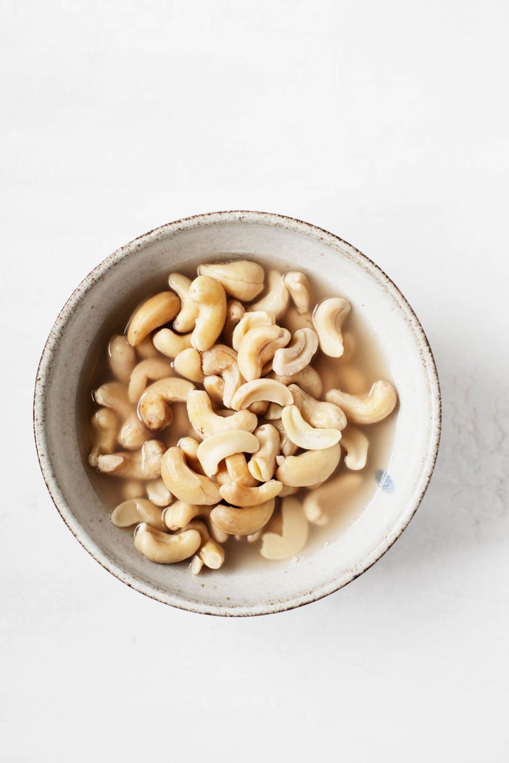 Raw cashews soak in a bowl of warm water.