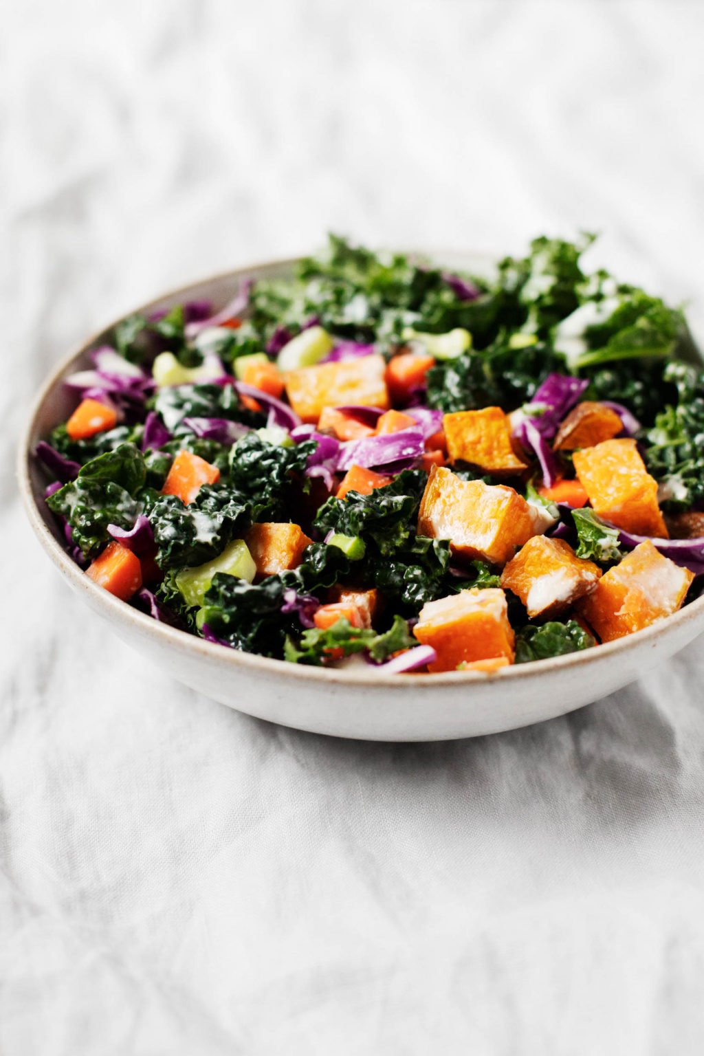 An angled photograph of a bowl of colorful winter greens and assorted vegetables.