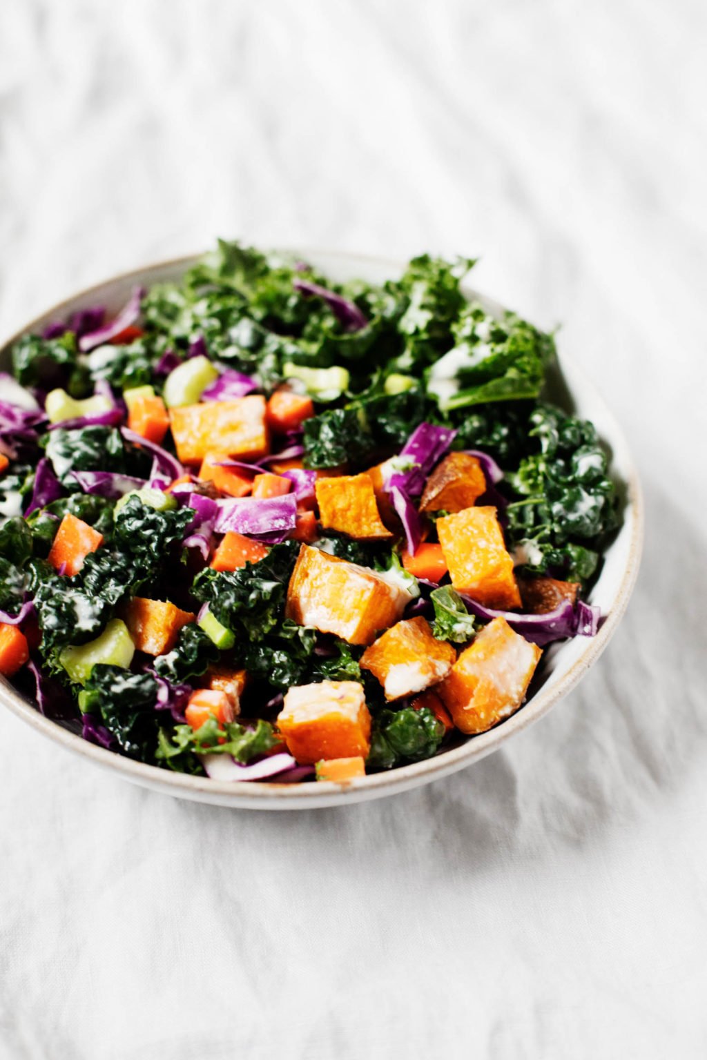 A serving bowl contains a colorful, plant-based kale salad.