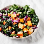 A serving bowl contains a colorful, plant-based kale salad.