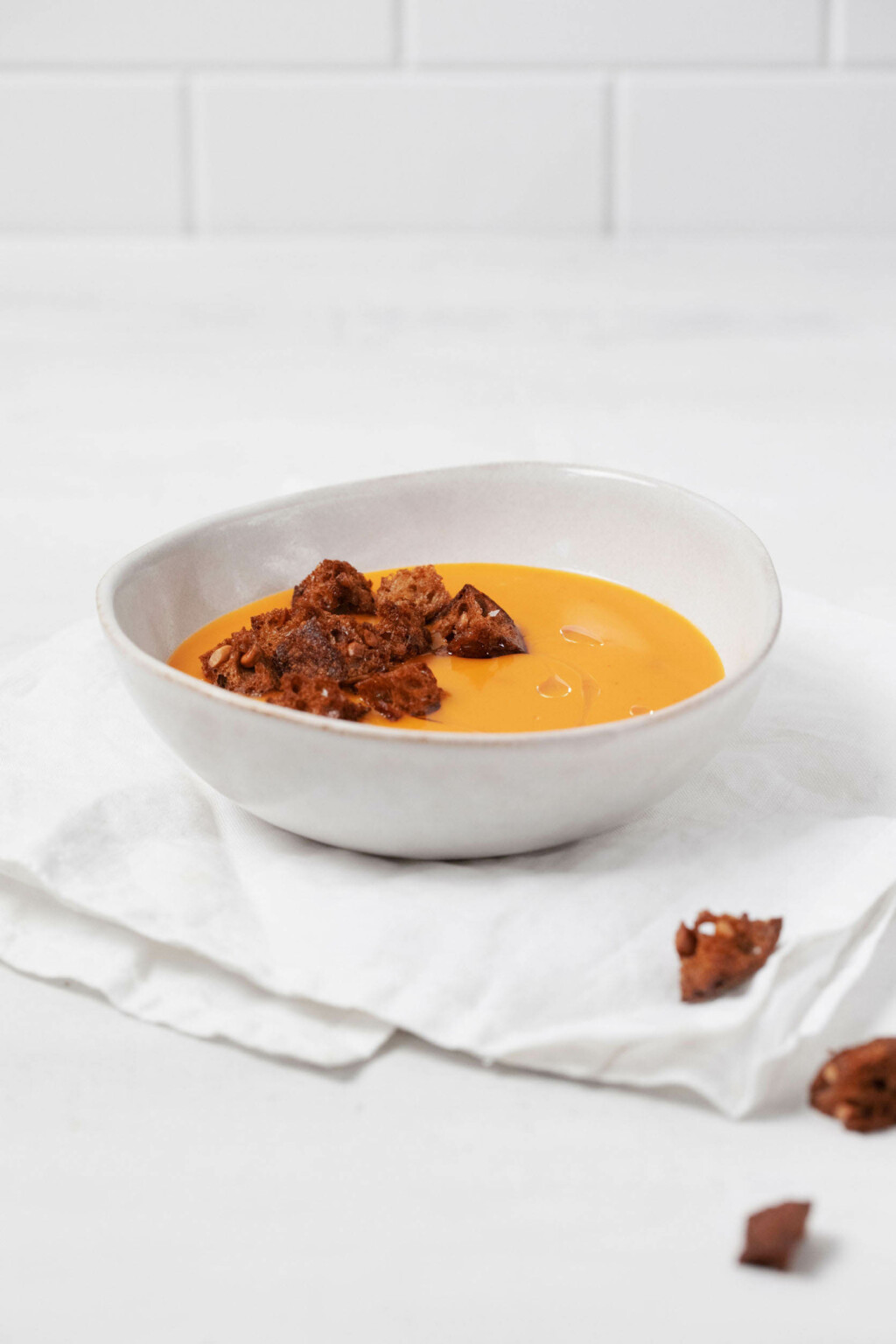 An asymmetrical, round bowl is resting on a light linen cloth. The bowl contains a creamy vegan butternut squash soup.