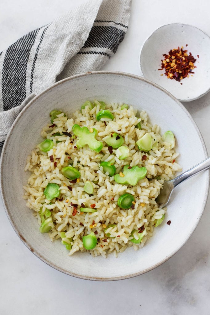 An overhead shot of a simple broccoli stem and brown rice stir fry, garnished with crushed red pepper flakes.