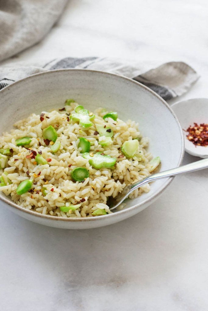 A bowl of vegan stir fry with thinly sliced broccoli stems, brown rice, seasonings, and a pinch of red pepper flakes.