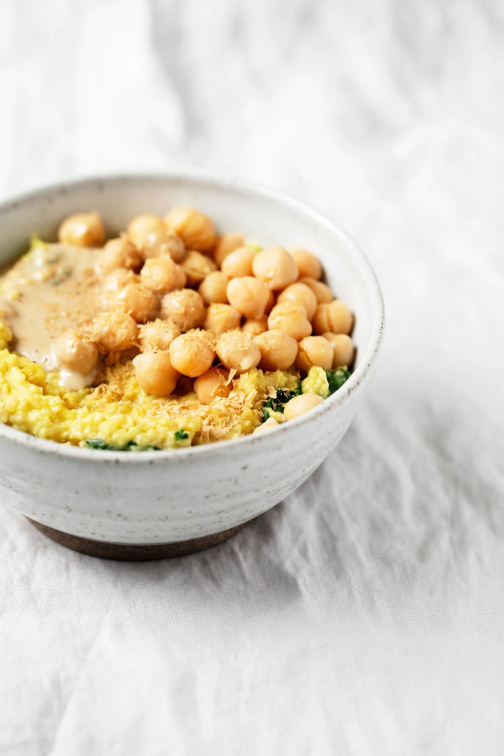 An angled shot of a bowl of savory oatmeal, which has been topped with tahini and chickpeas.
