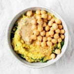 A bowl containing savory, turmeric spiced oats with chickpeas and greens is on a gray linen cloth.
