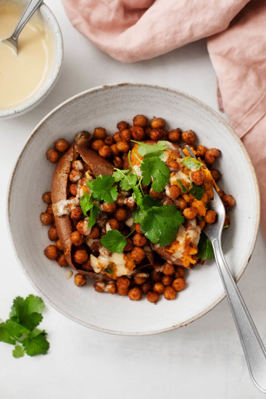 A bowl of stuffed sweet potatoes that have been topped with spice-roasted chickpeas, herbs, and a drizzle of tahini sauce.