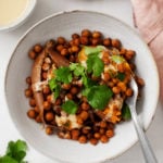 A bowl of stuffed sweet potatoes that have been topped with spice-roasted chickpeas, herbs, and a drizzle of tahini sauce.