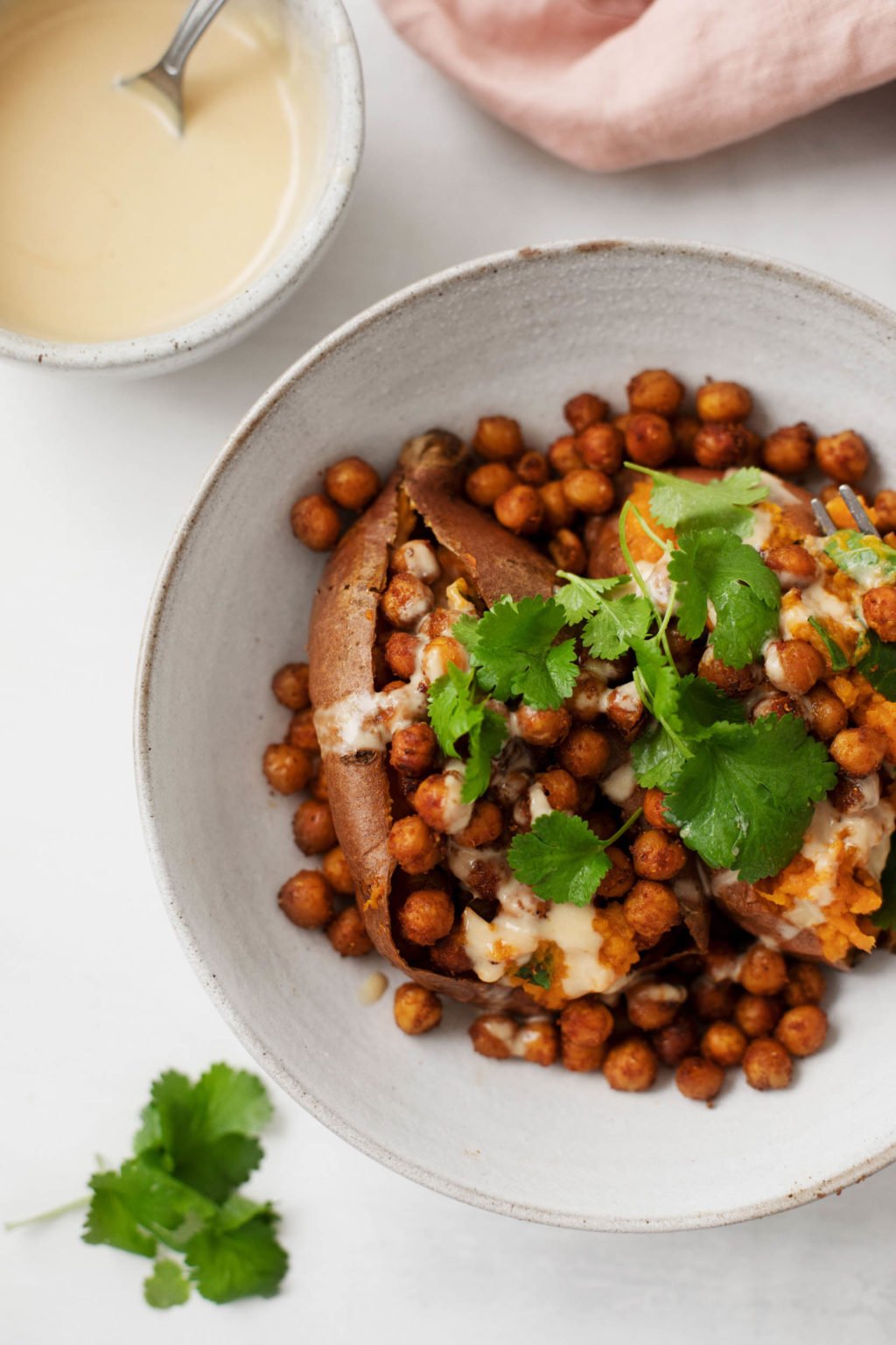 A zoomed in image of a Tandoori spiced sweet potato, stuffed with chickpeas, fresh cilantro, and a drizzle of tahini lime sauce. 