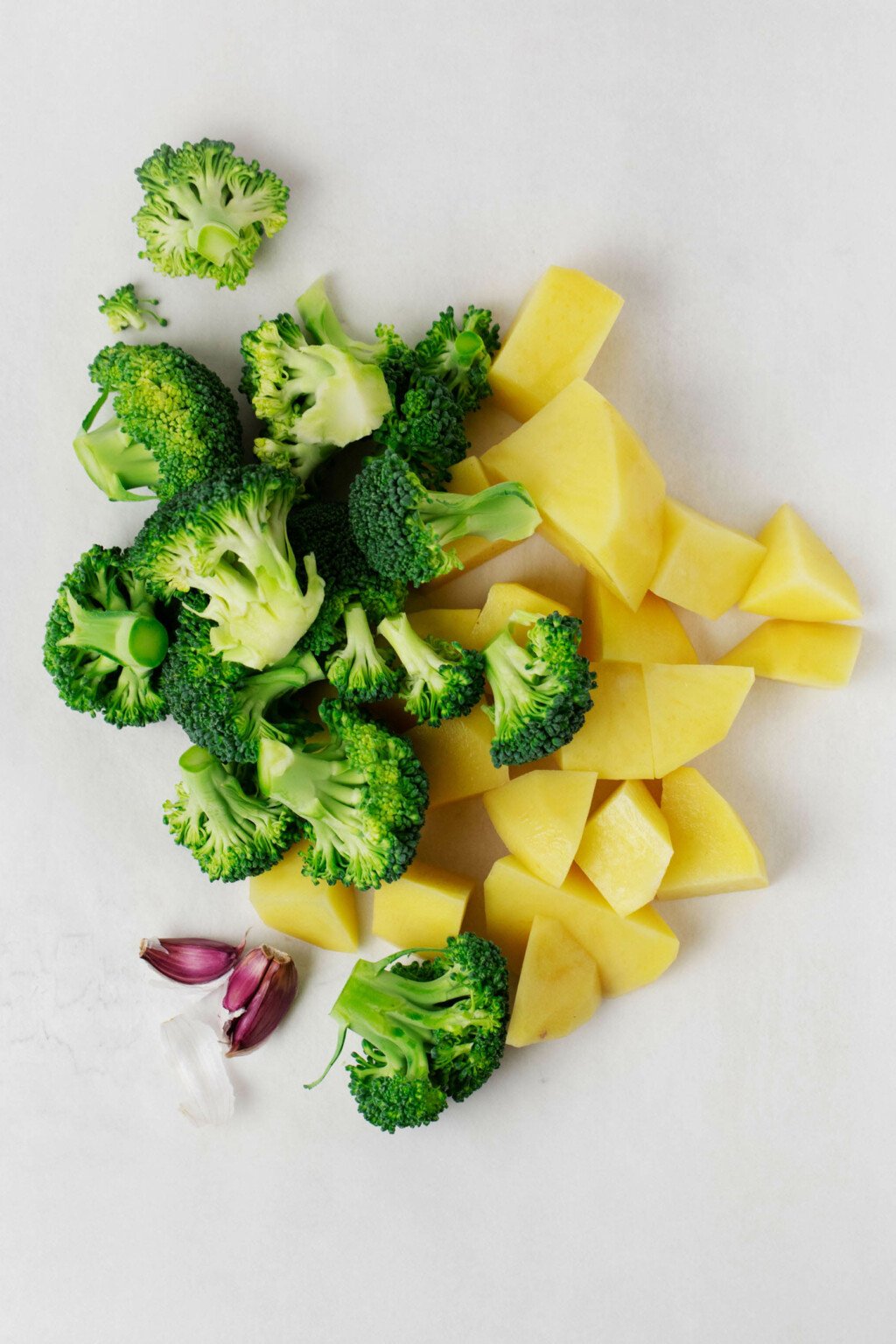 Potatoes, broccoli and garlic are laid out on a white surface.