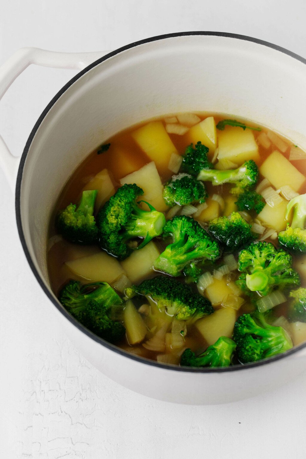 A soup pot holds potatoes, broccoli, and broth.