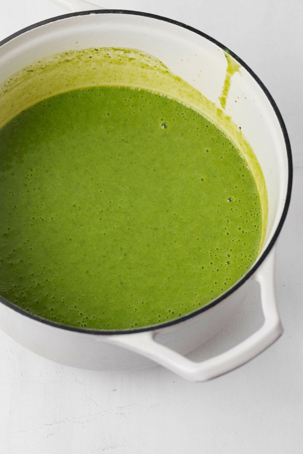 A simple green soup is being warmed in a white soup pot with a dark rim.