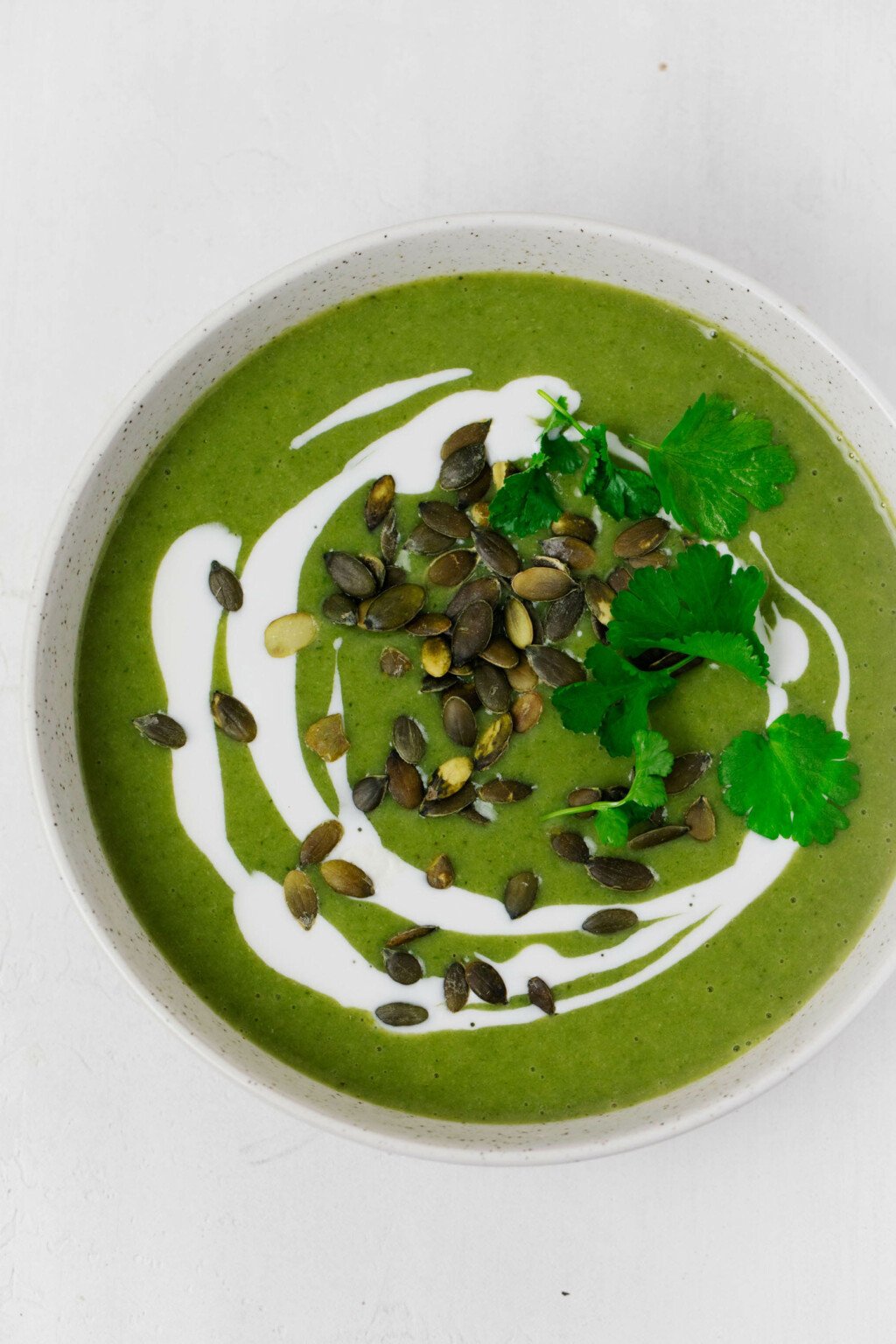 A bowl of simple green soup is topped with pumpkin seeds, cashew cream, and herbs.