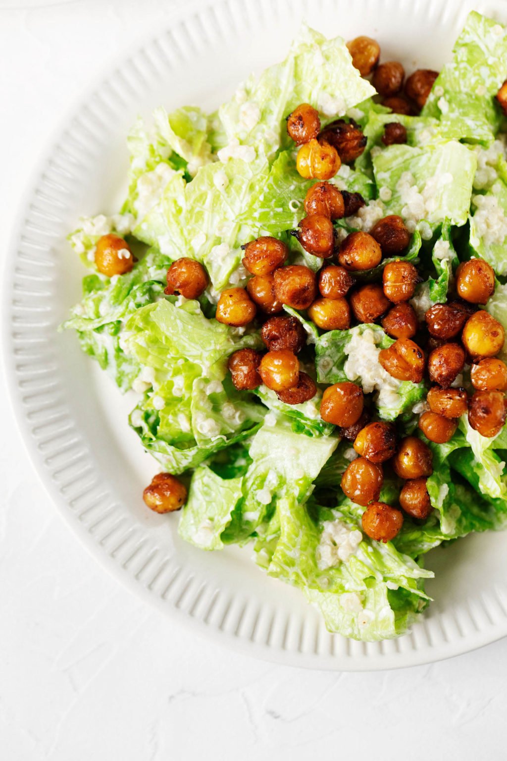 An overhead image of a white, fluted plate, which has been topped with vegan Caesar salad and roasted chickpeas.