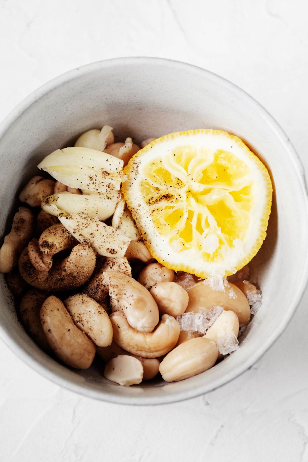 A small, white pinch bowl holds creamy white beans, squeezed lemon, and garlic.