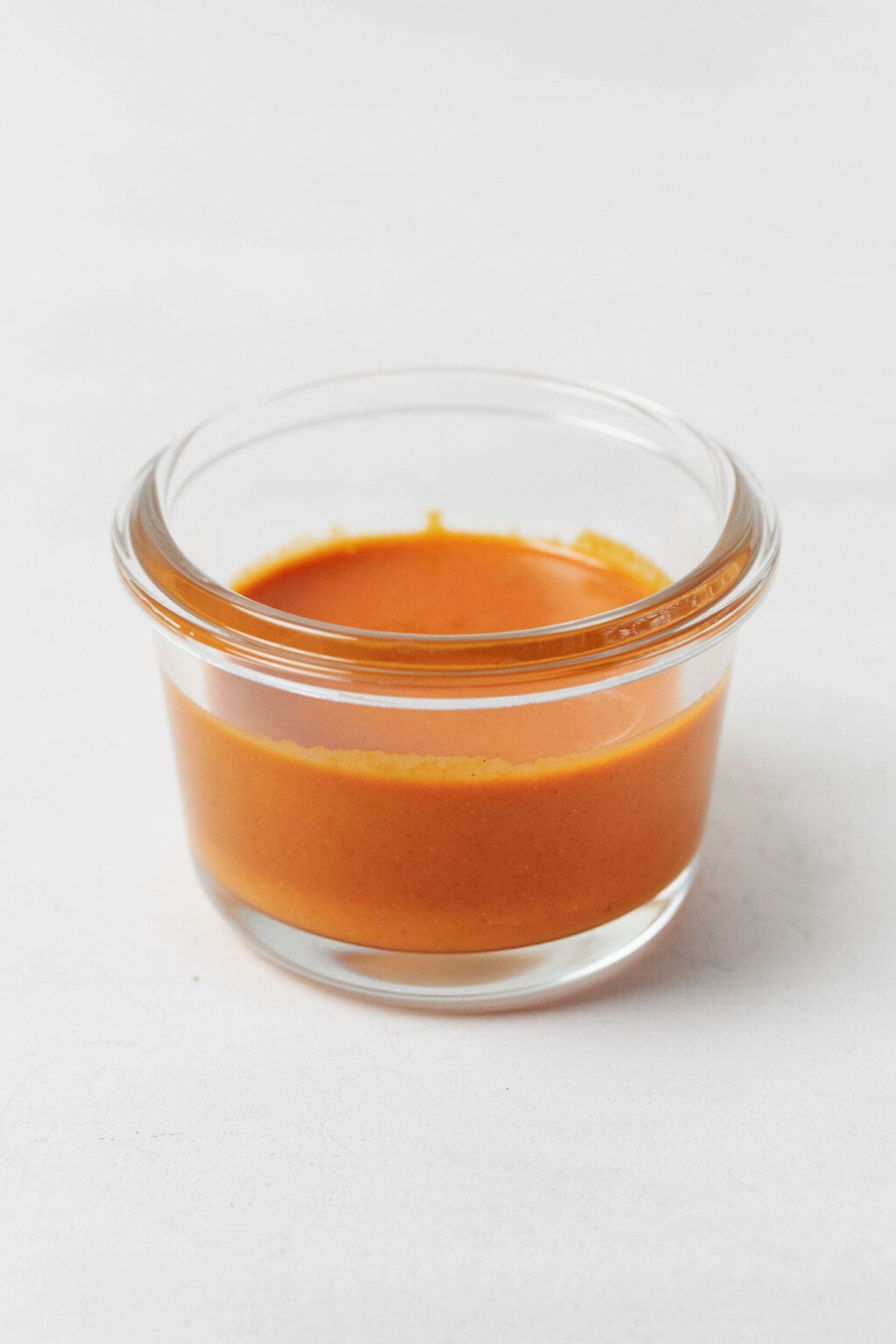 A small, glass container with an orange sauce is resting on a white container.