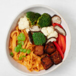 Red curry noodle bowls rest in asymmetrical bowls on top of a white surface.