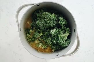 A large, gray pot is filled with broth, potatoes, and leafy greens.