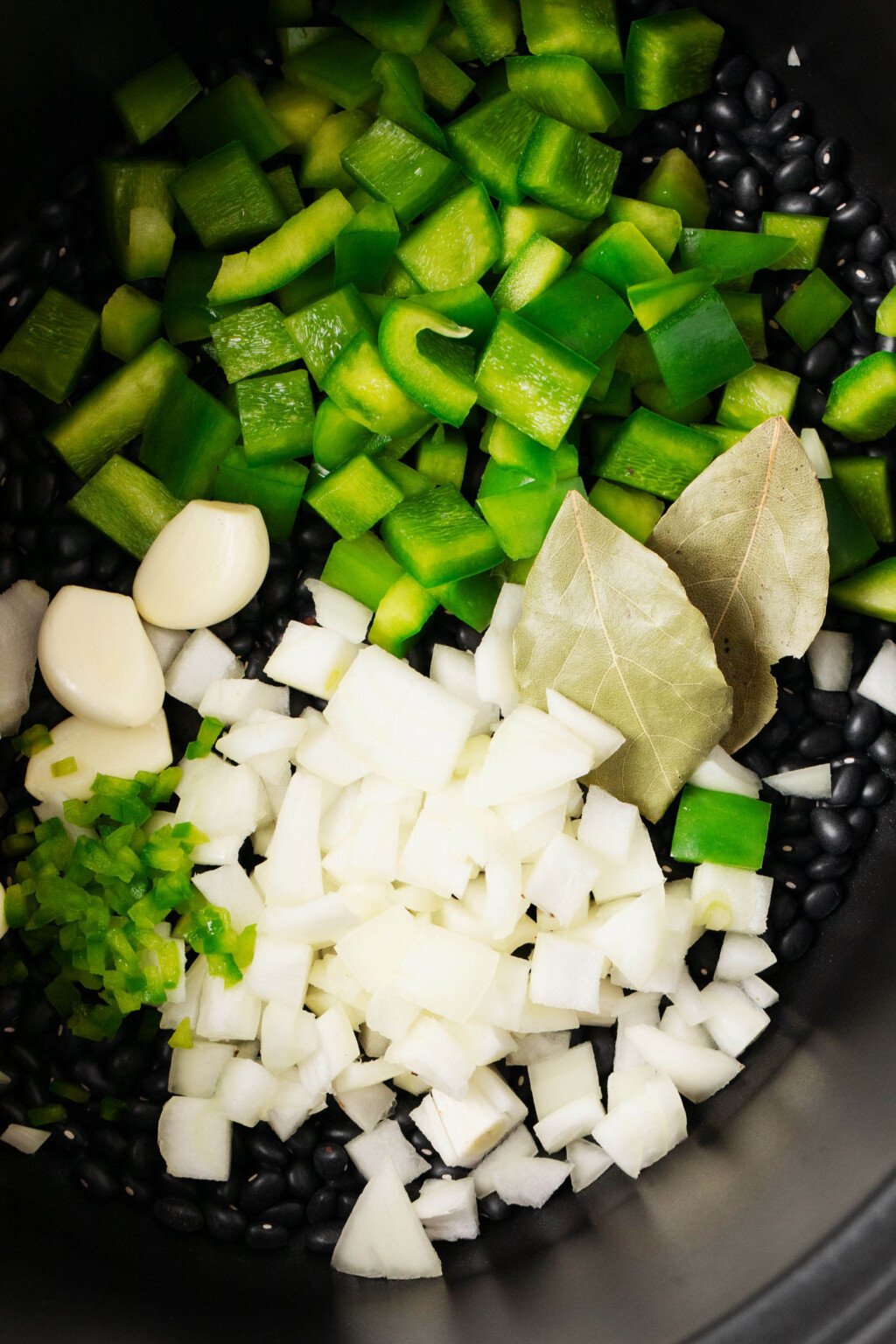 A zoomed-in, overhead image of chopped pepper, onion, whole garlic cloves, and bay leaves.